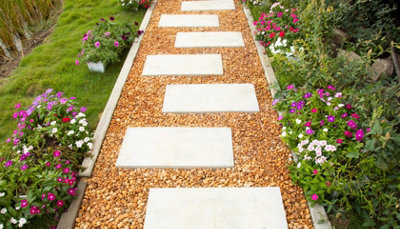 Square stepping stones arranged in a staggered pattern over light brown pebbles, creating a distinctive and eye-catching garden pathway.