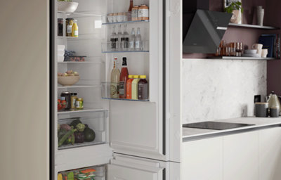 Open, well-stocked fridge beside a marble-effect worktop.