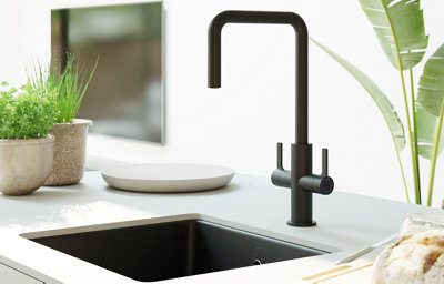 Close up of a large black sink with matching black tap, mounted on a bright white worktop.