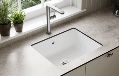 White inset sink with a chrome tap on a light stone-effect worktop.