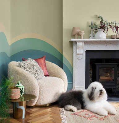 A cosy living room corner with a hand-painted mural that in shades of blue that complements the curves of an armchair.
