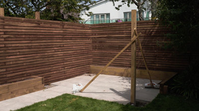 Post which has been installed in the ground is supported by two pieces of timber. The timber supports are screwed into the post, they then run diagonally to the ground where they are weighed down.