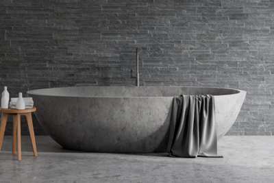 Grey bathroom with grey textured metro wall tiles behind a large freestanding grey bathtub.