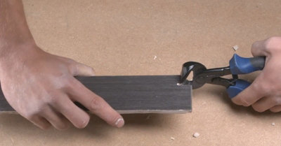 Person squeezing a pair of tile nippers which are positioned on top of a tile to remove a small section.