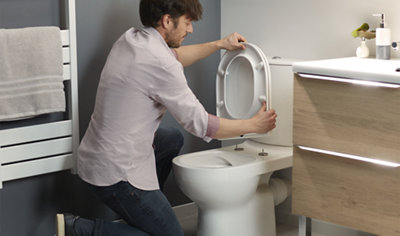 Person placing a toilet down onto two toilet seat fixings which have been installed on the toilet.