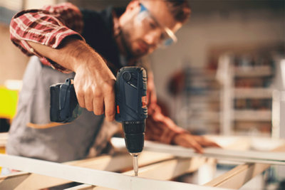 Man with goggles in check shirt drilling into a piece of wood with a power tool