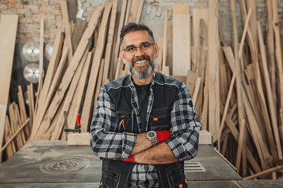 Smiling man in check shirt standing in a workshop full of timber