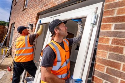 Two tradespeople fitting glass doors into a house.