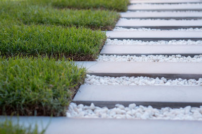 A distinctive garden pathway with two different-sized rectangular stone slabs over white gravel, some extending into the grass, creating an artistic and captivating focal point.