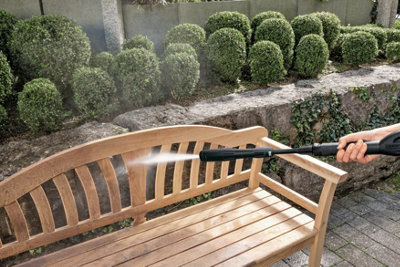 Using a pressure washer to clean a wooden garden bench.