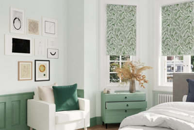 White and green bedroom with white walls, green panelling on lower half of wall, green bedside table, white armchair and a statement gallery wall above the armchair.