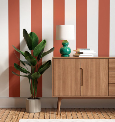 White and orange striped wallpaper in a living room with a mid century modern wooden sideboard and a large houseplant.