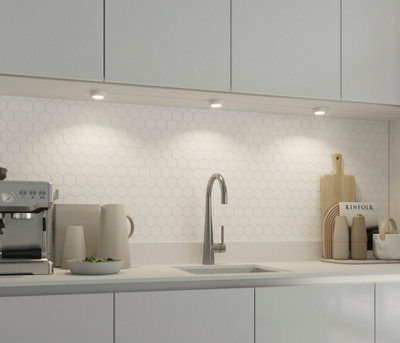 A white kitchen with a hexagon tiled white splashback and under cabinet lights.