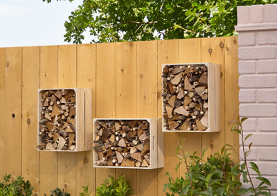 3 crate log holders full of small logs mounted on a wood fence.