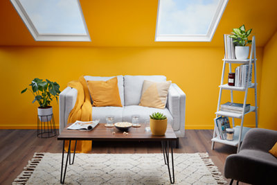 Yellow living room, with a white fabric sofa in the centre with a potted plant to the left and a modern bookshelf to the right.