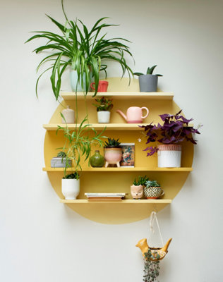 A circular wall feature with shelves painted in a sunny yellow centre, fading into lighter shades on either side, creating a unique ombre effect to showcase decorative items.