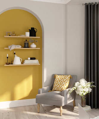 A white living room with a curved alcove painted in sunny yellow, creating a vibrant backdrop for shelves and decorative accessories.