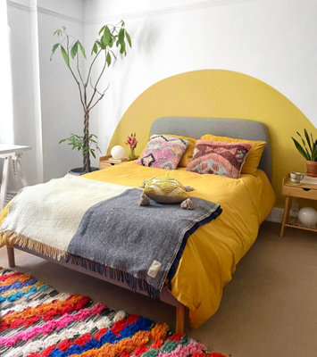 A bedroom with a bold curved yellow mural painted behind the bed, creating the illusion of a large, statement headboard with a sunset-inspired design.