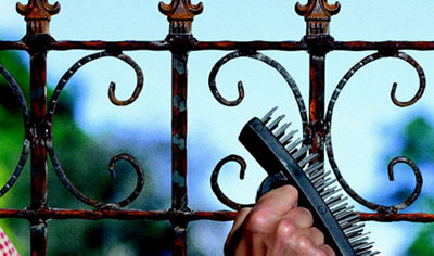 A person using a wire brush on a metal railing to remove rust and smooth the surface in preparation for painting.